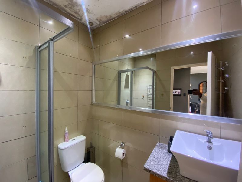 Compact bathroom featuring a vessel sink, granite vanity, shower enclosure, and tiled walls. Note visible ceiling water damage requiring repair.