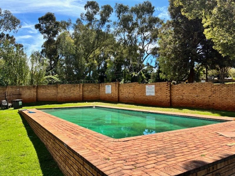 Communal swimming pool area featuring a brick-paved surround, perimeter brick wall, and surrounding lawn space.