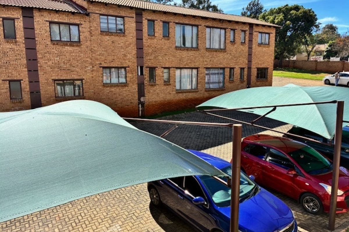 Exterior view of a multi-story brick apartment complex featuring a paved parking area with installed shade cloth carports.