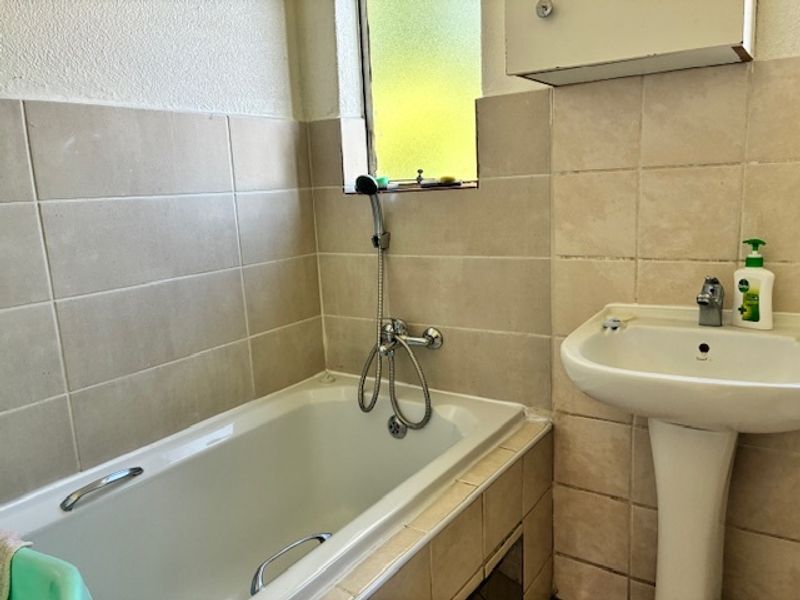 A functional bathroom featuring a bathtub with a handheld shower attachment, a pedestal sink, and neutral wall tiling.