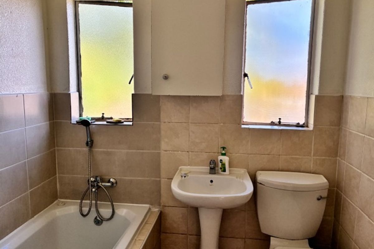 A functional bathroom featuring a bathtub, pedestal basin, toilet, and wall-mounted cabinet, finished with neutral wall tiling and dual frosted windows.