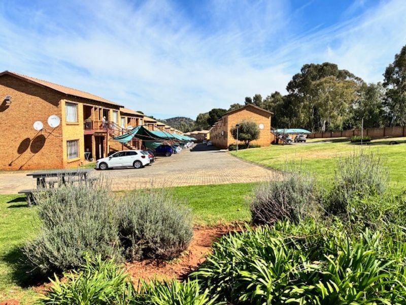 Exterior view of a residential apartment complex featuring brick buildings, paved parking areas with carports, and well-maintained communal garden spaces.