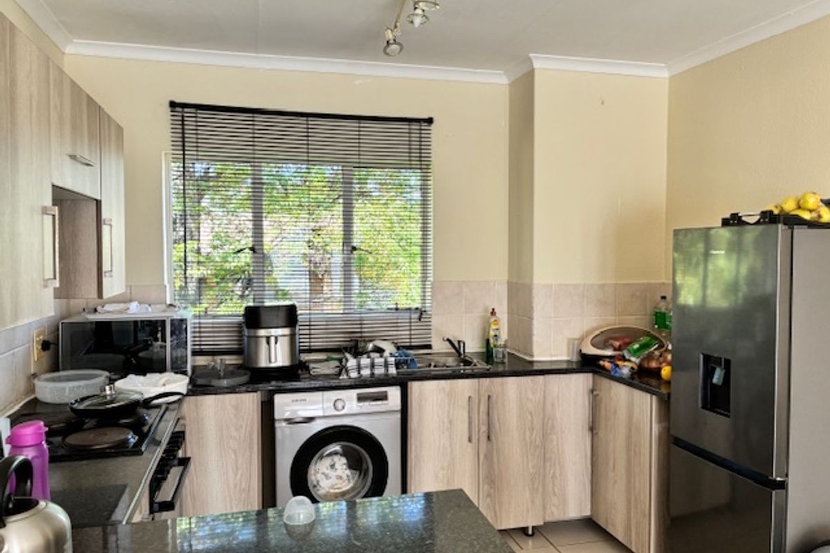 Functional kitchen featuring light wood-look cabinetry, dark granite countertops, tiled backsplash, and integrated laundry facilities with a window view.