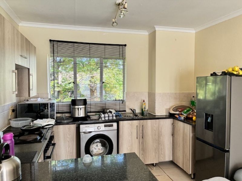 Functional kitchen featuring light wood-look cabinetry, dark granite countertops, tiled backsplash, and integrated laundry facilities with a window view.