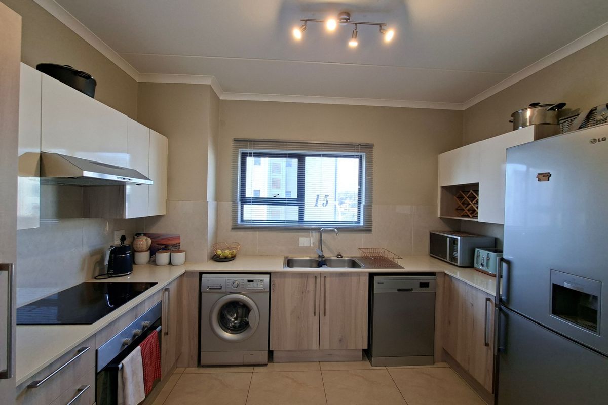 A modern, well-maintained kitchen featuring light wood-finish cabinetry, integrated appliances, a double sink, and a tiled backsplash with ample counter space.
