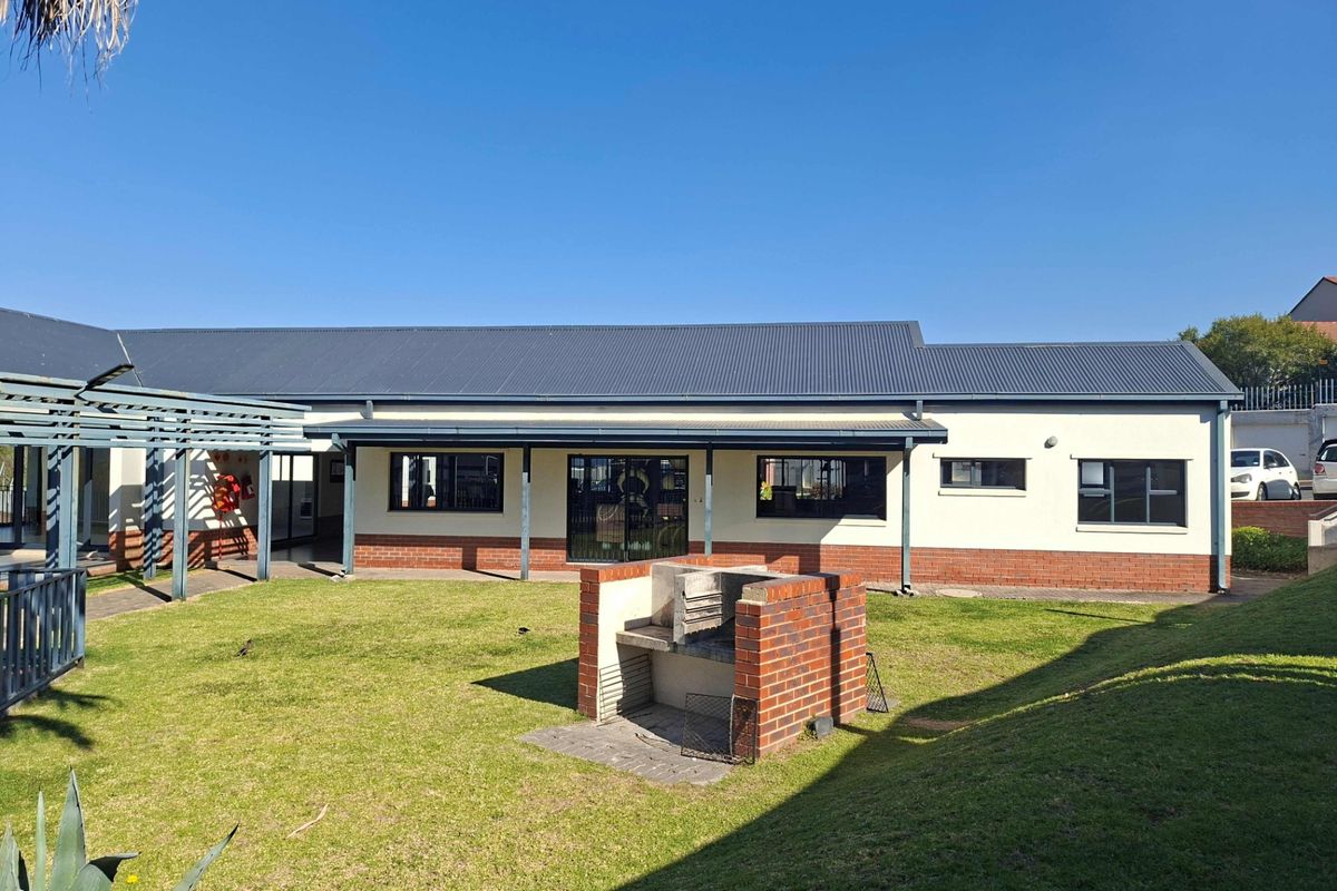 Rear view of the apartment building featuring a well-maintained lawn, a brick built-in braai area, and a covered pergola walkway.