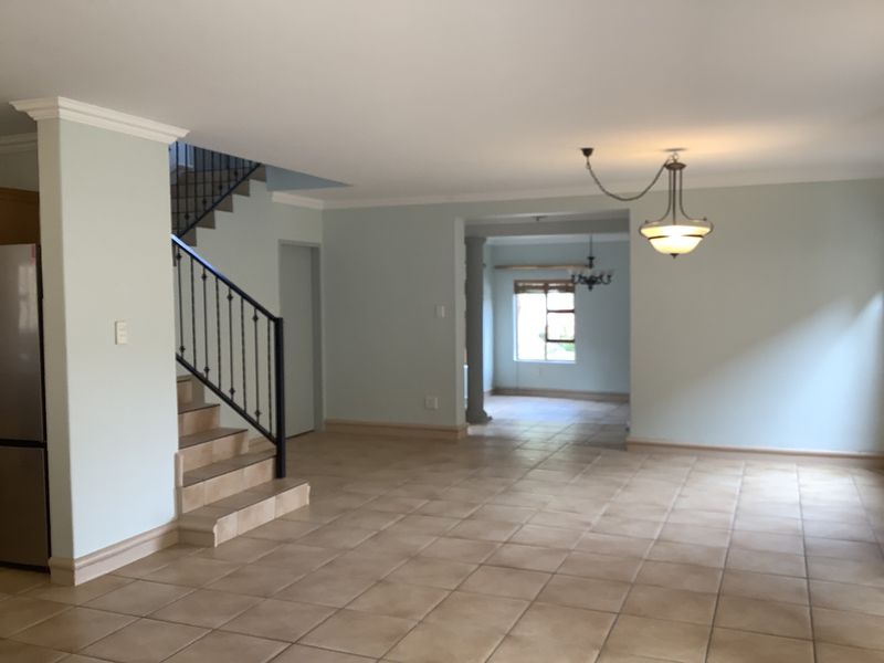Spacious open-plan living area featuring tiled flooring, a wrought iron staircase, and neutral wall tones, offering a versatile layout for modern living.
