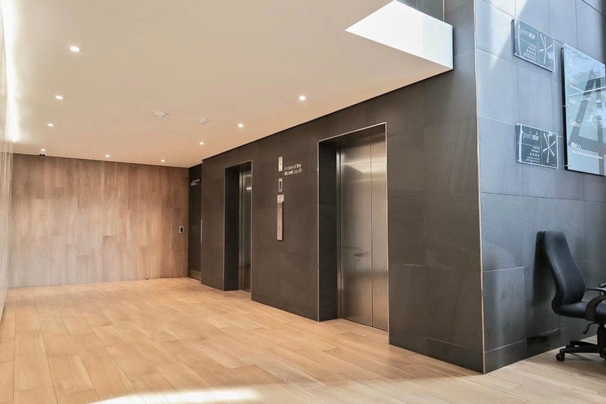 Modern commercial building lobby featuring stainless steel elevator banks, sleek tiled wall finishes, and high-quality wood-look flooring with recessed lighting.