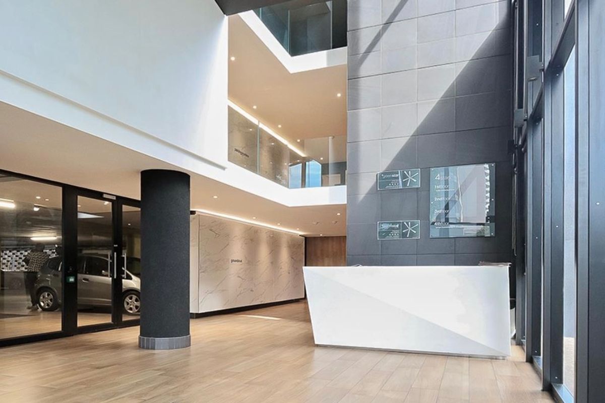 Modern commercial building lobby featuring a sleek reception desk, marble-look wall finishes, and an open-plan atrium with glass balustrades and high-quality floor tiling.