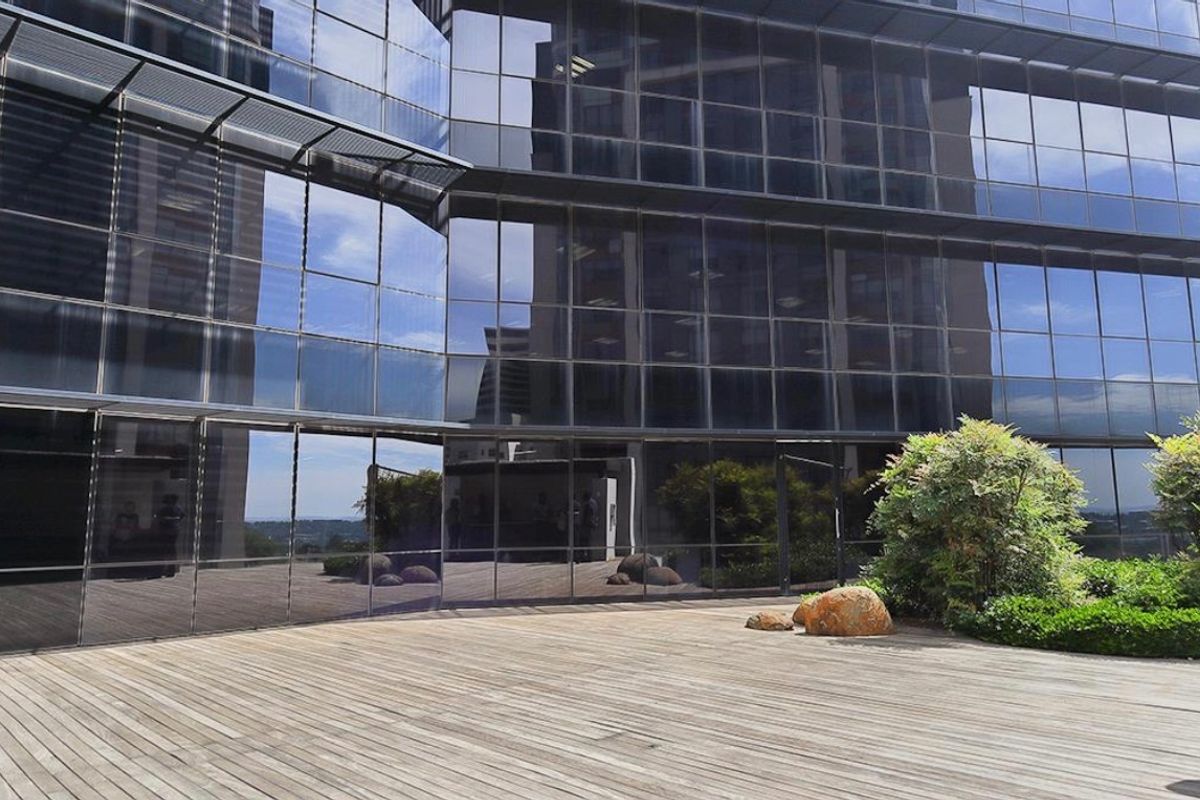 Modern commercial building exterior featuring a glass curtain wall facade and a spacious timber deck area with landscaped garden elements.