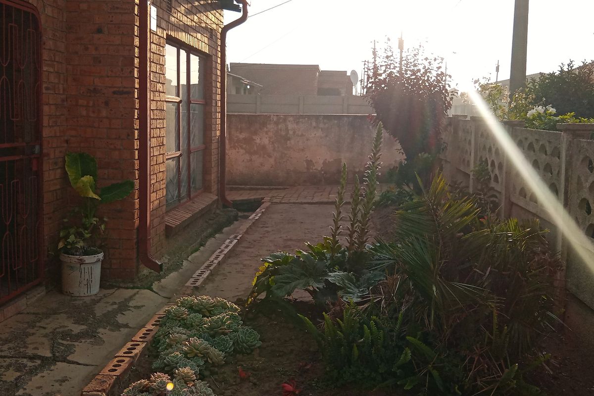 A side view of the property featuring a face brick exterior, a precast concrete boundary wall, and a paved walkway leading to a security gate.