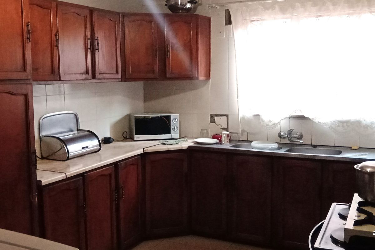A dated kitchen featuring traditional wooden cabinetry, a double basin sink, and tiled backsplash, offering potential for a modern renovation.