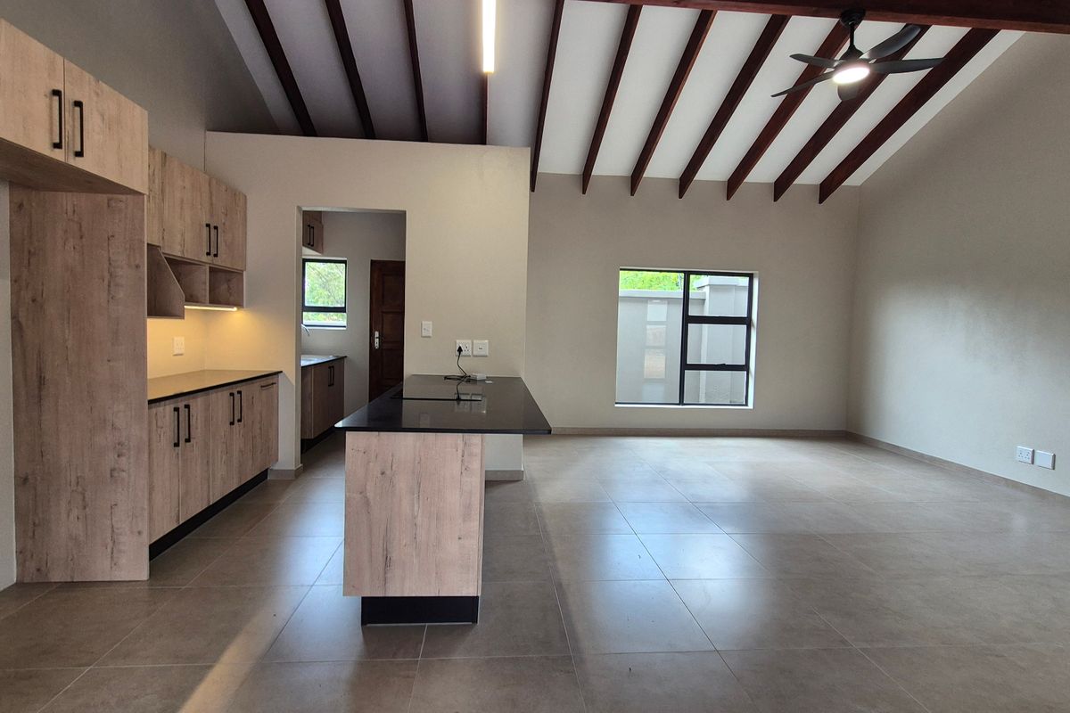 Spacious open-plan kitchen and living area featuring modern wood-finish cabinetry, a central island, tiled flooring, and exposed timber ceiling beams.