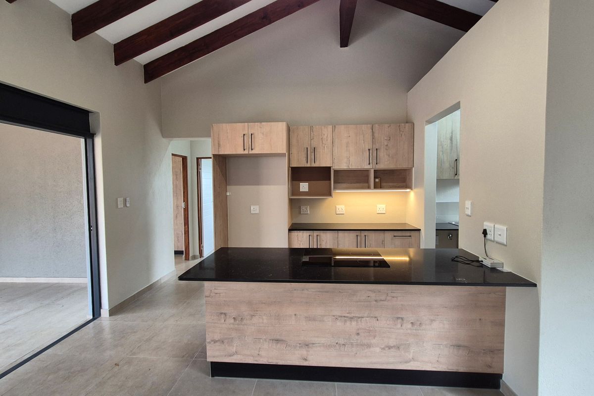 Modern kitchen featuring light wood cabinetry, a central island with a stone countertop, integrated hob, and striking exposed timber beams under a vaulted ceiling.