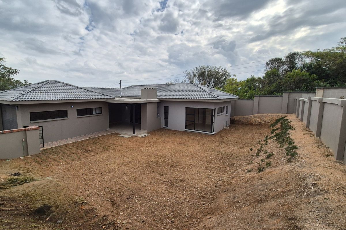 Rear view of a modern single-story house featuring a tiled roof, covered patio, and a large, unlandscaped backyard enclosed by a perimeter wall.
