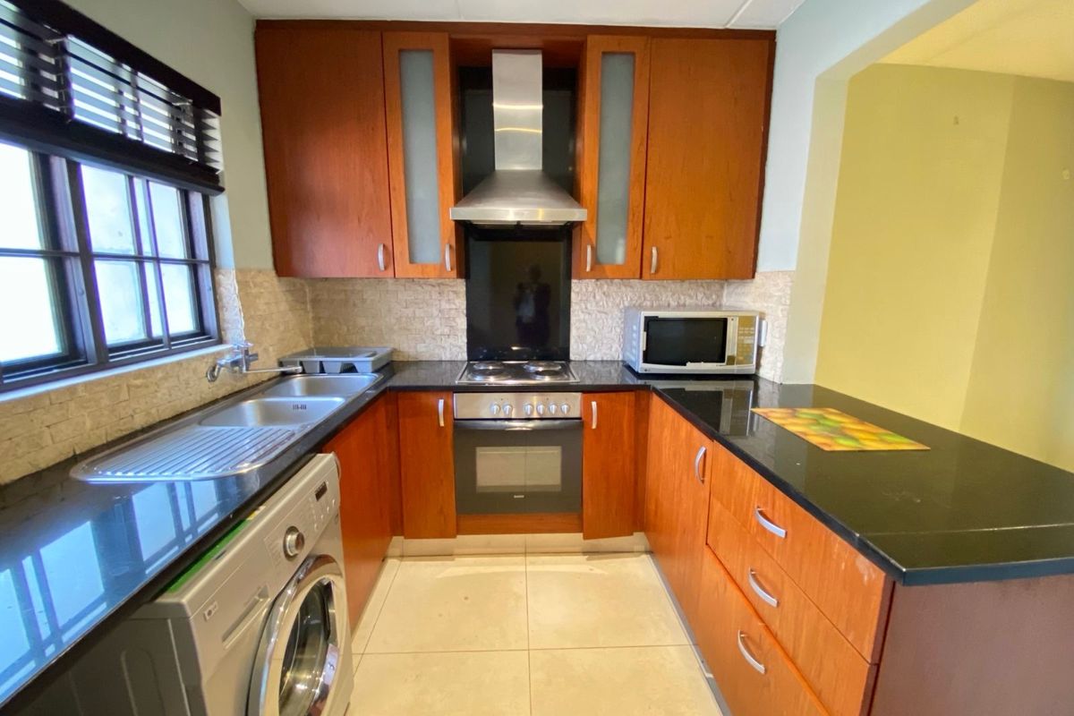 A functional kitchen featuring wood-finish cabinetry, granite countertops, a built-in oven with extractor fan, and tiled flooring.