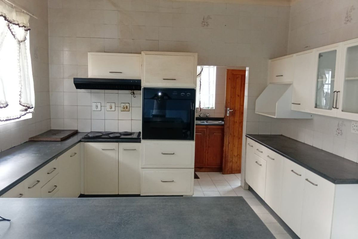 A functional kitchen featuring built-in cabinetry, an integrated oven, electric hob, and dark countertops, offering a dated aesthetic ready for modernization.