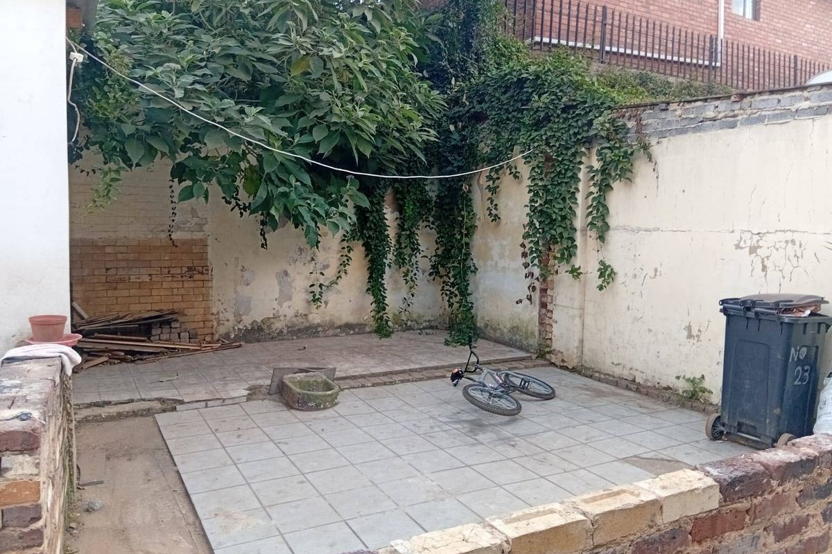A rear courtyard area featuring a tiled patio, stone basin, and high boundary walls with climbing vegetation, requiring maintenance and cosmetic updates.
