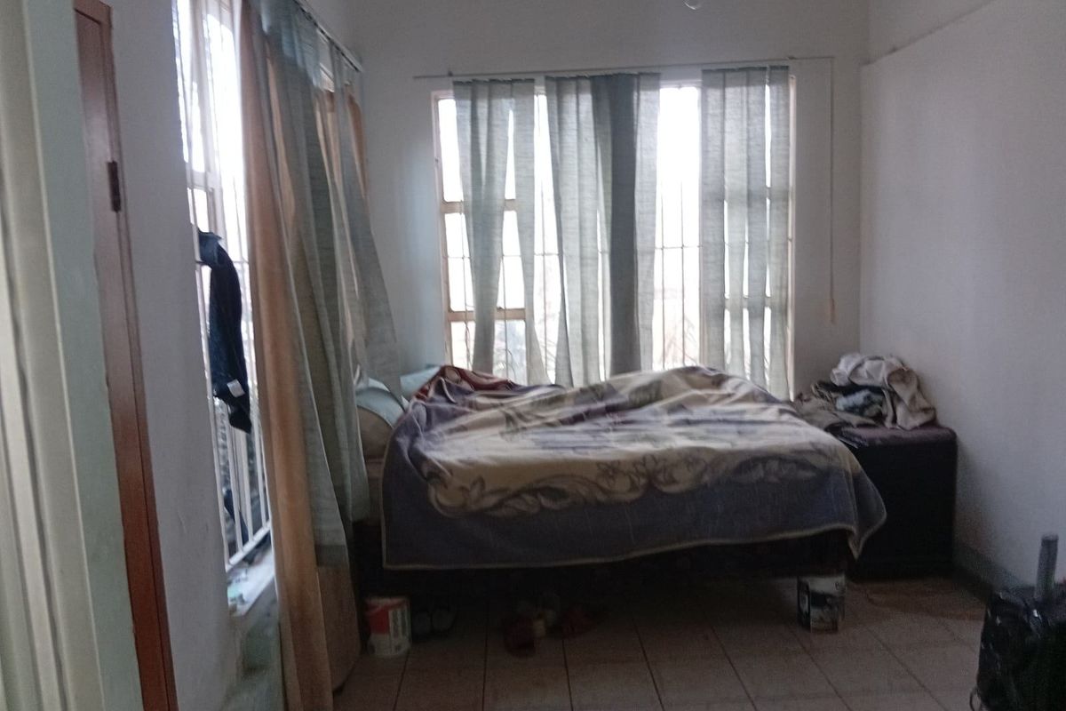 A bedroom featuring tiled flooring and large windows with security bars, requiring cosmetic updates to improve its overall condition and appeal.