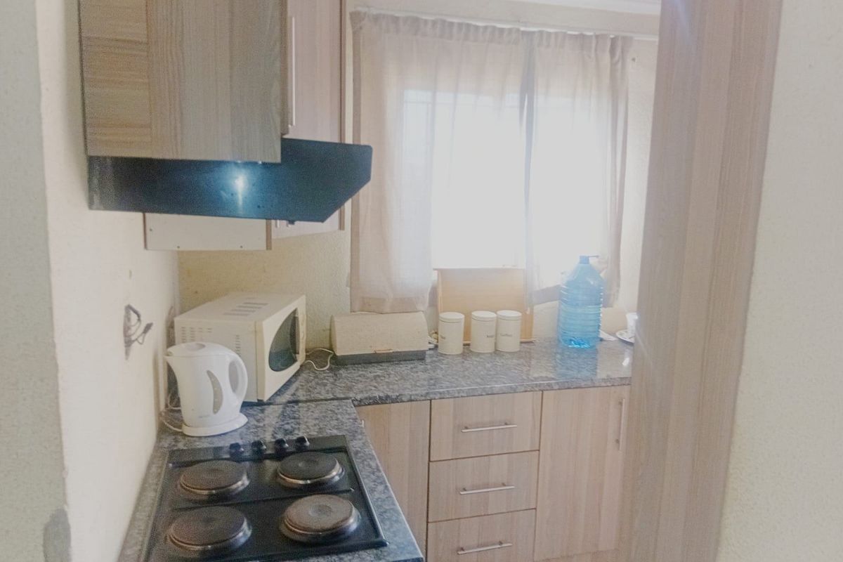 A compact kitchen featuring laminate cabinetry, a granite-look countertop, and a built-in electric hob with an extractor fan.