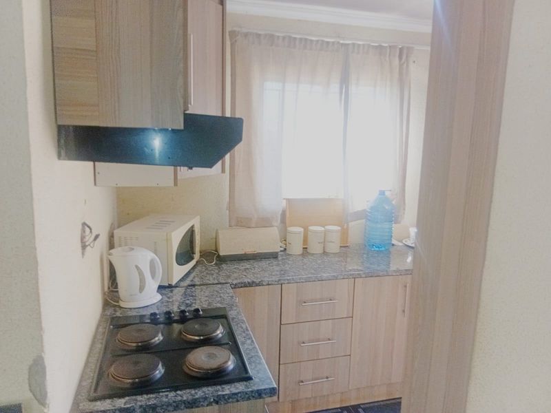 A compact kitchen featuring laminate cabinetry, a granite-look countertop, and a built-in electric hob with an extractor fan.