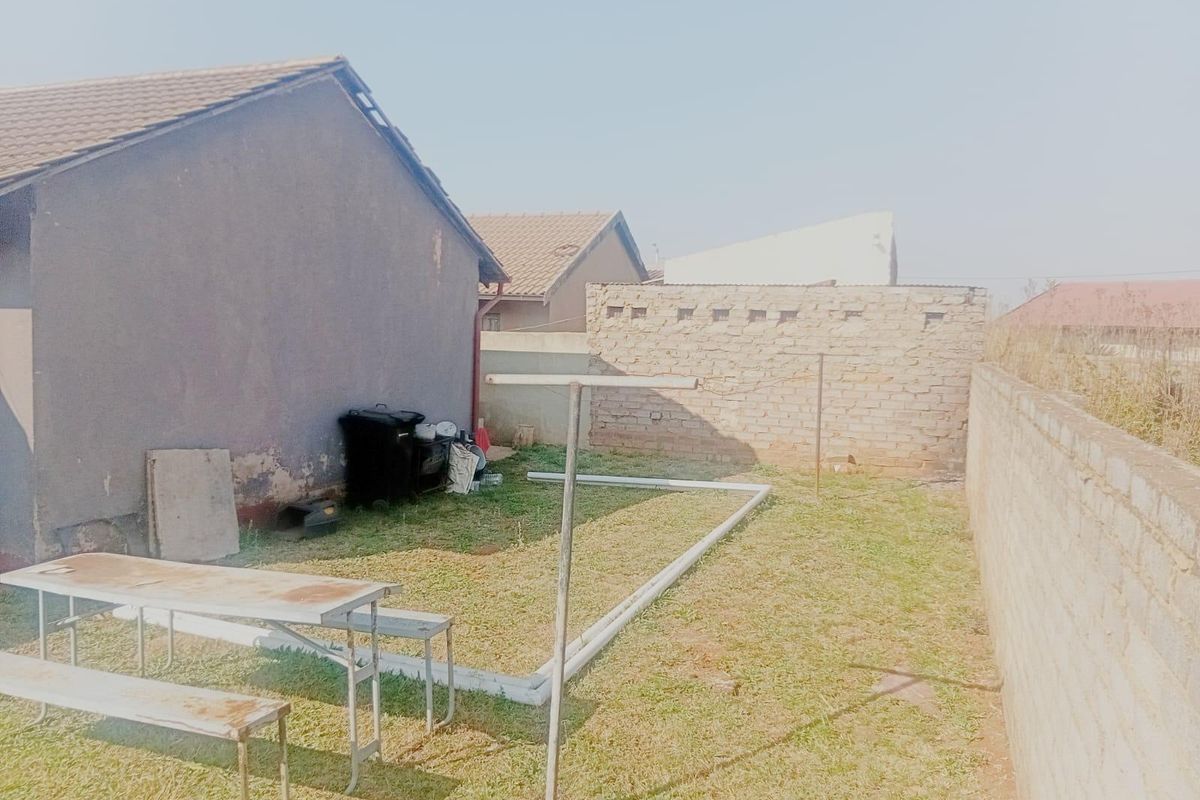 A rear exterior view of the property featuring a small lawn area, brick boundary walls, and a tiled roof structure.