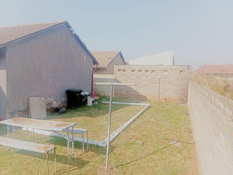A rear exterior view of the property featuring a small lawn area, brick boundary walls, and a tiled roof structure.