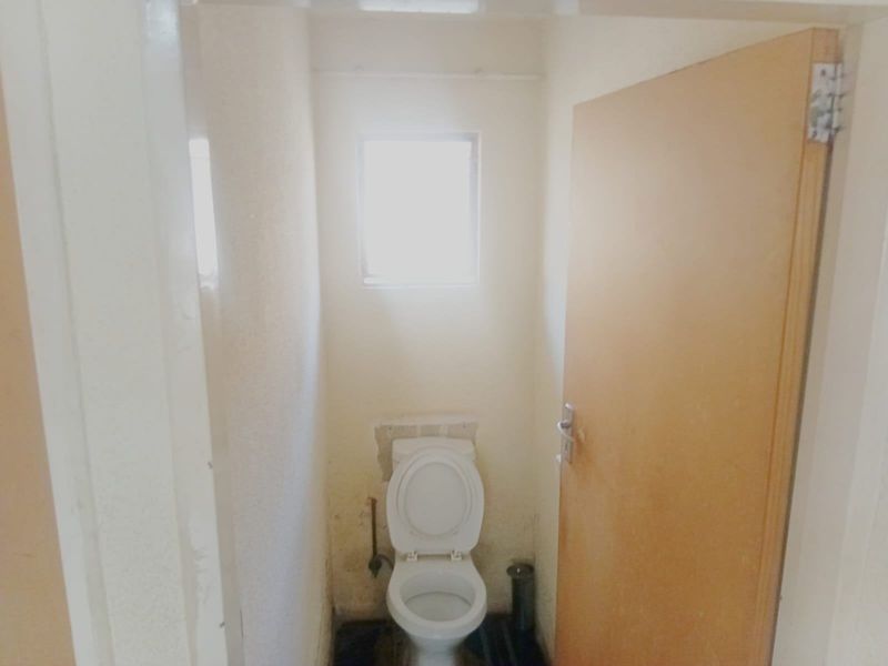 A small, dated bathroom featuring a standard toilet and window, requiring cosmetic updates and repairs to wall and floor finishes.
