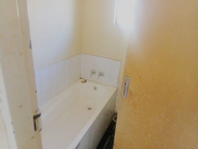 A compact bathroom featuring a standard bathtub with wall-mounted taps and a tiled splashback, requiring cosmetic updates to improve its overall condition.
