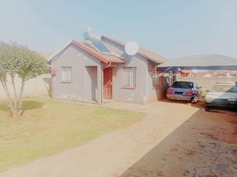 Front view of a detached house featuring a paved driveway, carport, solar water heater, and a front garden area.