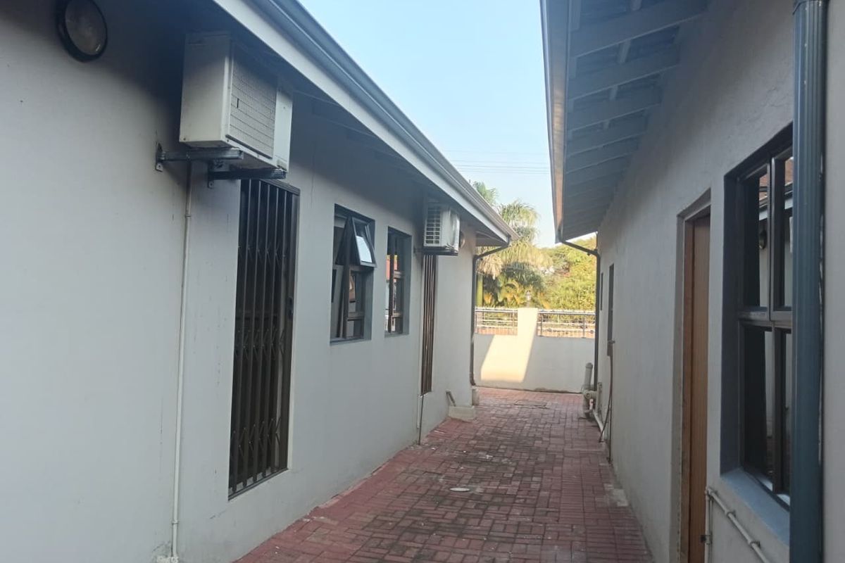 A side walkway between two building structures featuring paved flooring, security gates, and wall-mounted air conditioning units.