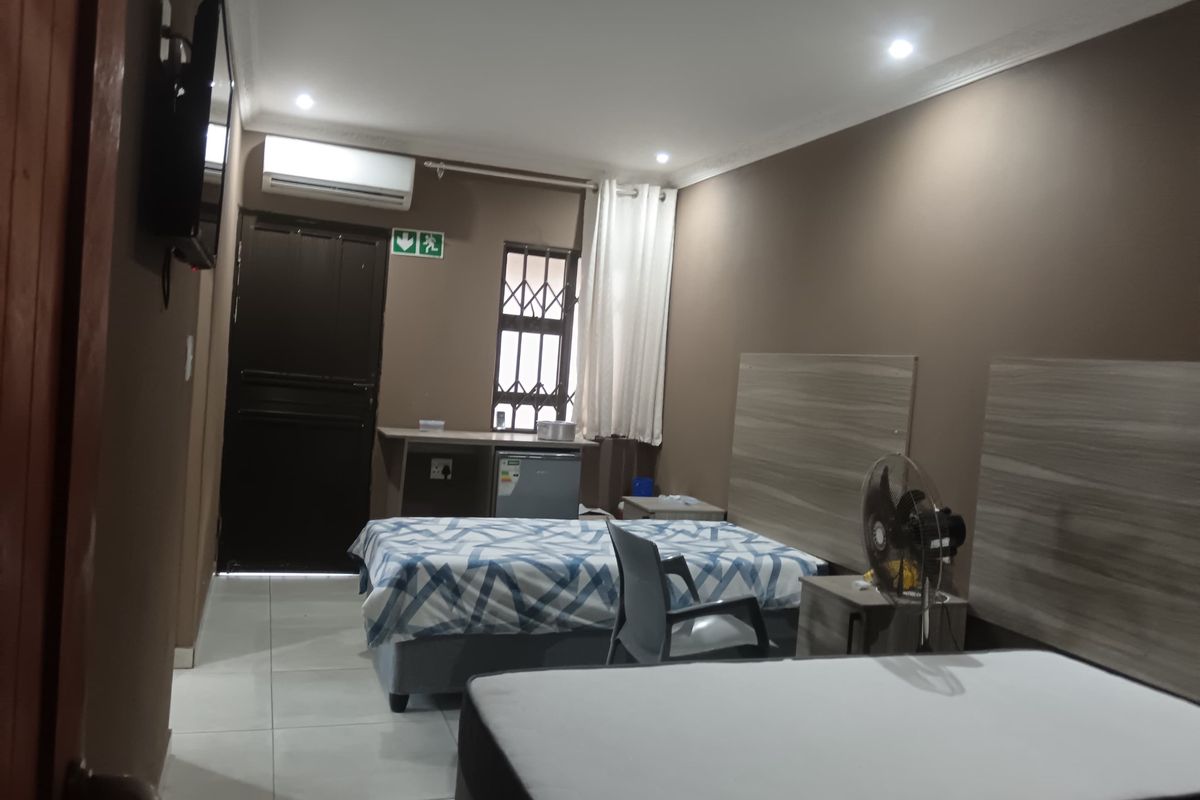 A functional bedroom featuring tiled flooring, recessed lighting, an air conditioning unit, and built-in headboards with a security gate on the window.