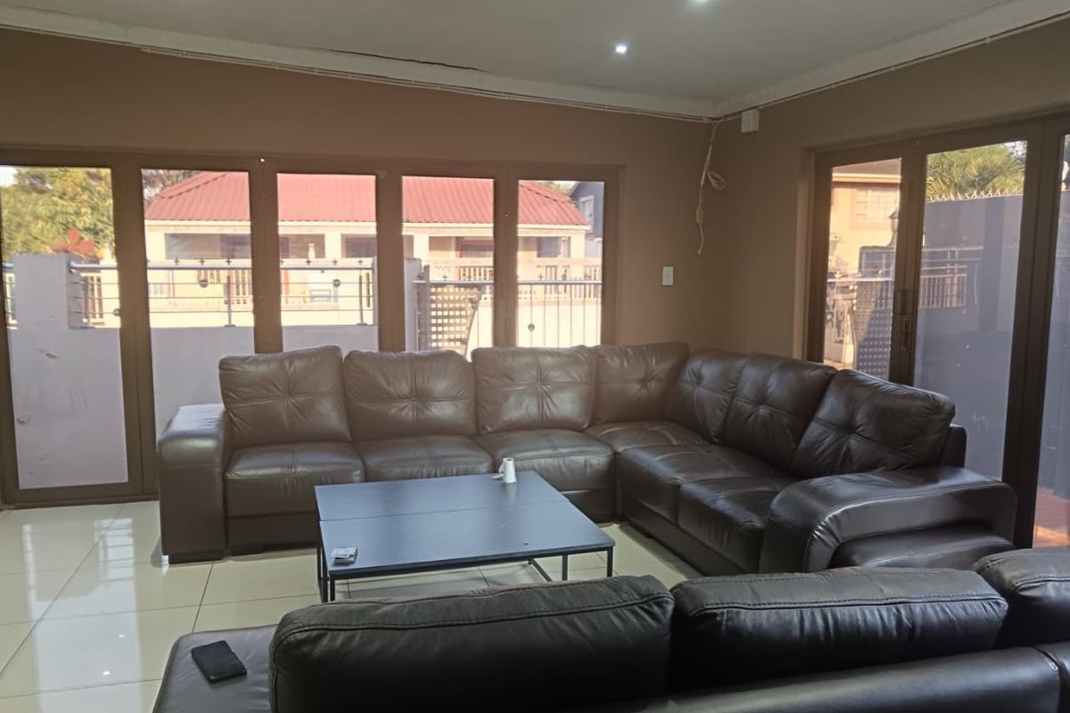 Spacious living room featuring large aluminium-framed glass sliding doors, tiled flooring, and recessed downlighting, offering a bright and open atmosphere.