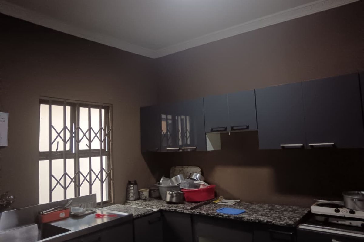 A functional kitchen featuring dark cabinetry, granite countertops, and a stainless steel sink, with security bars installed on the window.