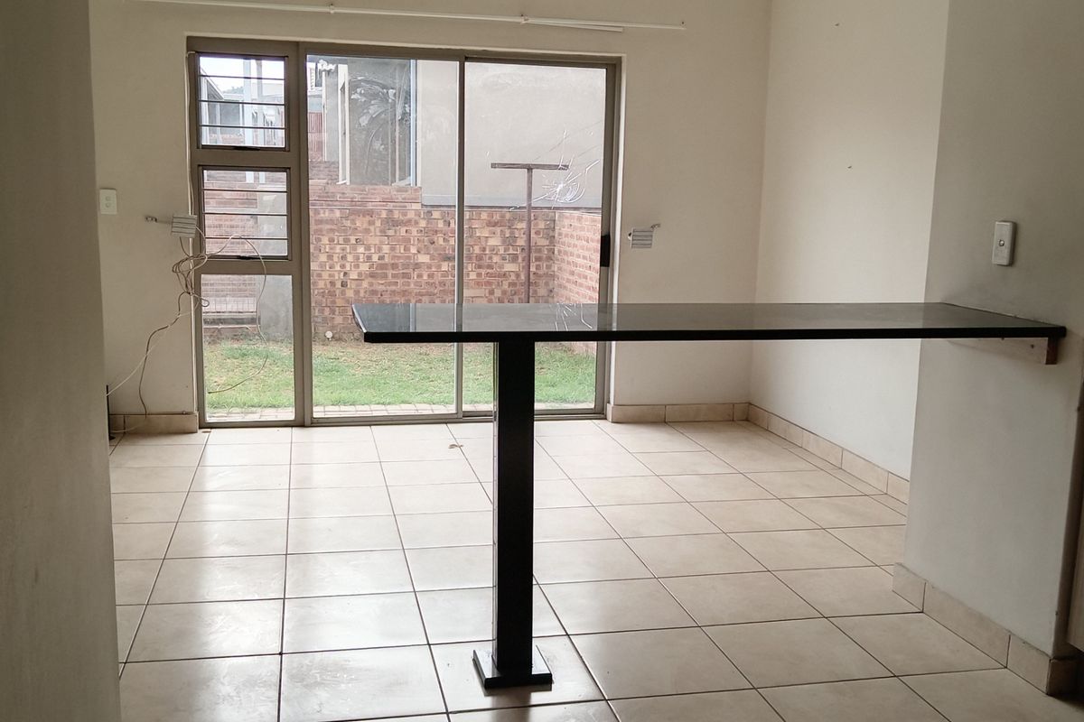 An empty open-plan living area featuring tiled floors, a built-in breakfast bar, and a sliding glass door leading to the rear garden.