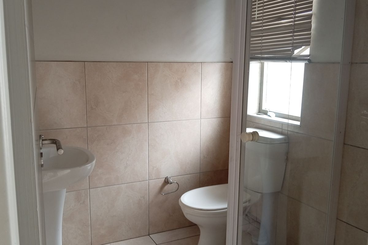 A functional bathroom featuring a pedestal basin, toilet, and neutral wall and floor tiling, providing a clean and practical space.