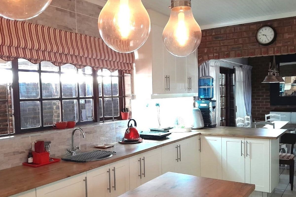 A charming kitchen featuring white shaker-style cabinetry, warm wooden countertops, a tiled backsplash, and an exposed brick feature wall.