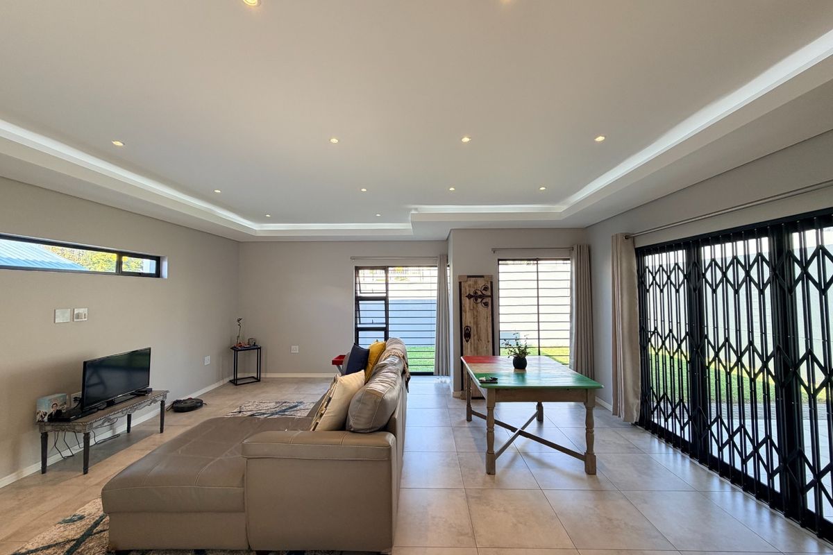 Spacious living area featuring tiled flooring, recessed ceiling lighting with cove accents, and large sliding glass doors with security gates leading outdoors.