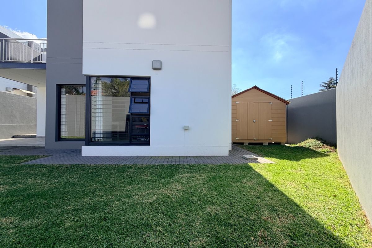 Rear view of the property featuring a paved patio area, well-maintained lawn, boundary walls with electric fencing, and a detached storage shed.