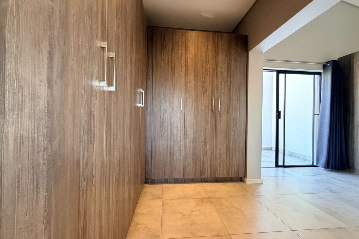 Spacious bedroom featuring extensive built-in wooden cabinetry, neutral tiled flooring, and a sliding glass door providing access to an outdoor area.