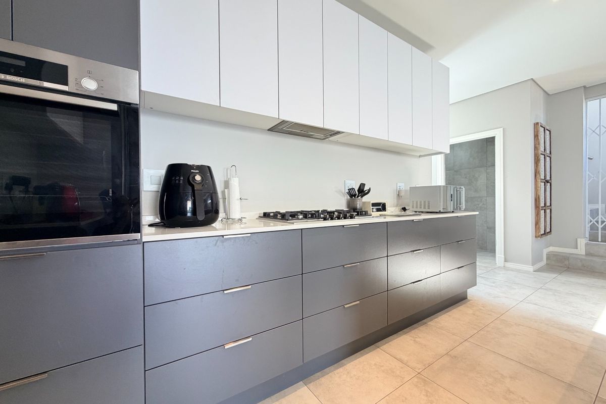Modern kitchen featuring sleek grey lower cabinetry, white upper cabinets, quartz countertops, built-in oven, and gas hob with integrated extractor fan.