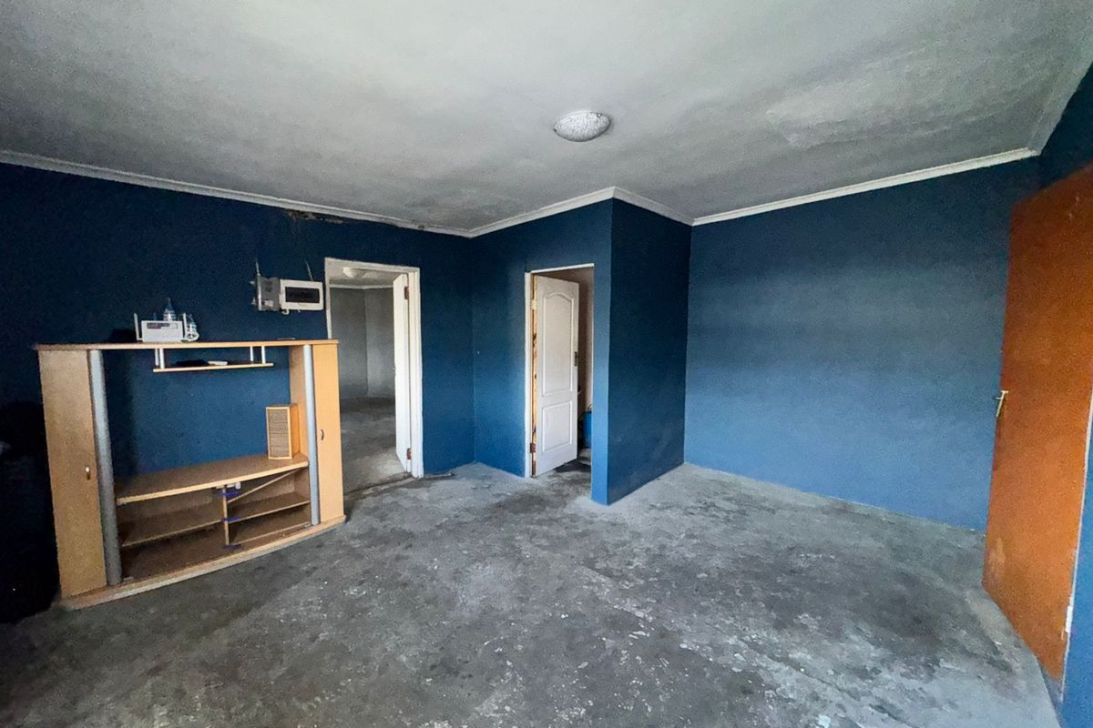 An empty living room featuring dark blue walls, exposed concrete flooring, and multiple internal doorways, requiring cosmetic updates and floor finishing.