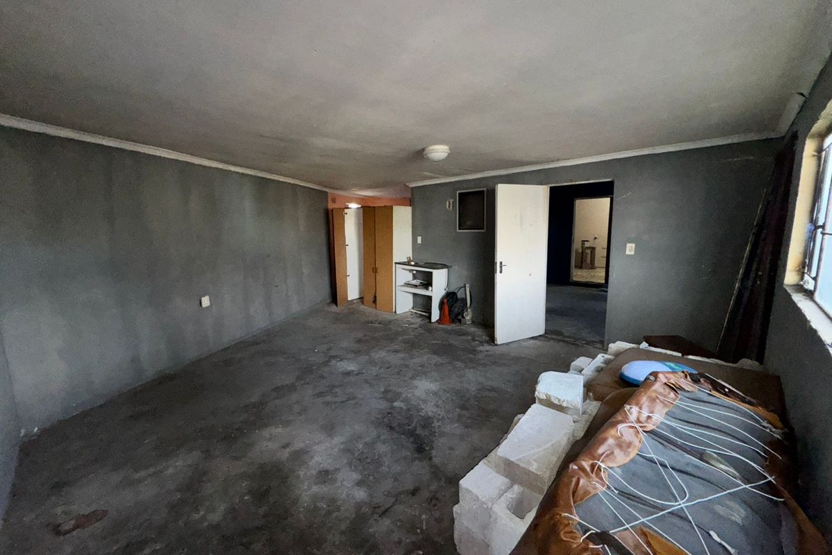 An empty, unfinished living area featuring grey walls, exposed concrete flooring, and a built-in cupboard, offering a blank canvas for renovation.