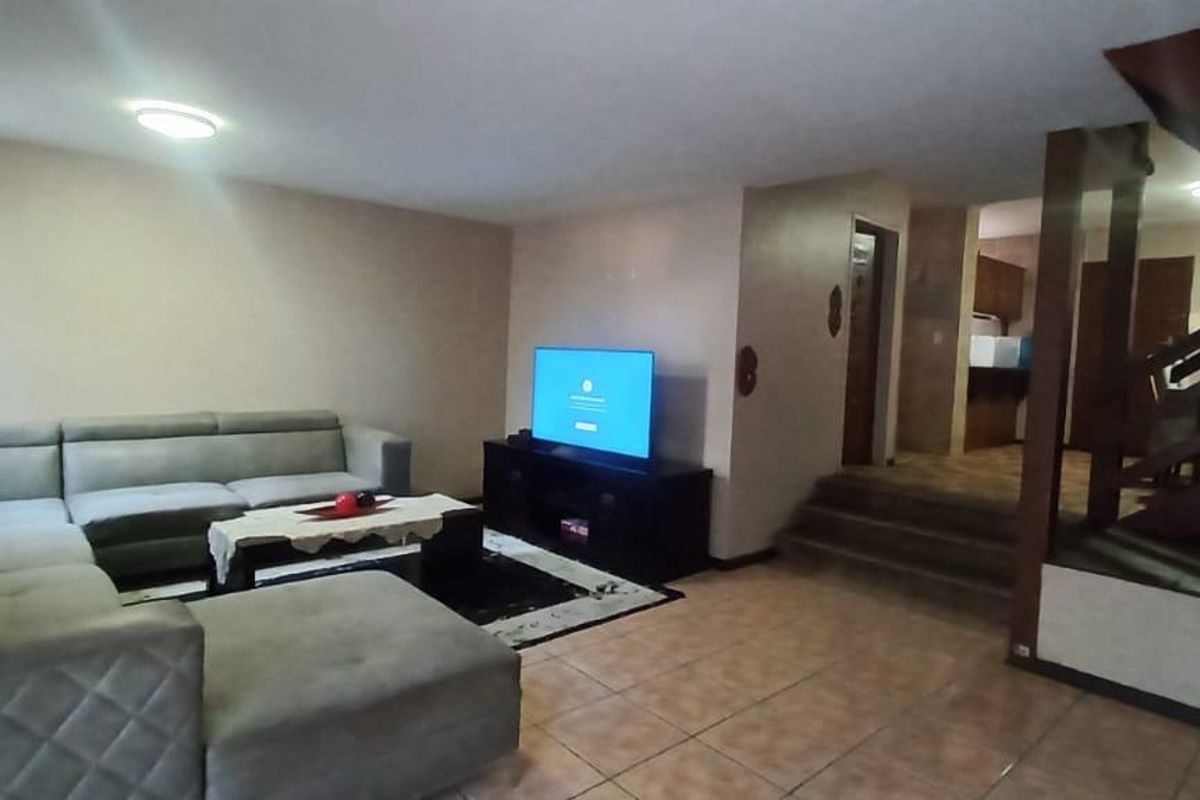 Spacious living area featuring tiled flooring and a prominent wooden staircase leading to the upper level, with an open flow to the kitchen area.