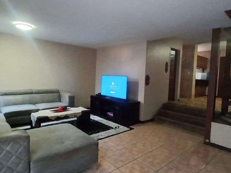 Spacious living area featuring tiled flooring and a prominent wooden staircase leading to the upper level, with an open flow to the kitchen area.