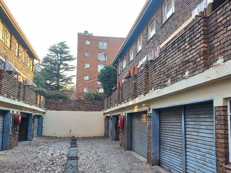 A view of a townhouse complex garage area featuring multiple roller shutter doors, brick construction, and a central cobblestone driveway with drainage.
