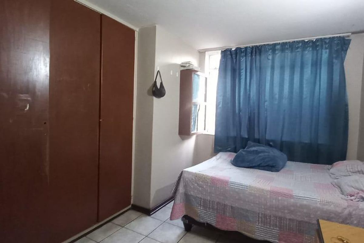 A bedroom featuring tiled flooring and a large built-in wardrobe, offering a functional space with potential for cosmetic updates.