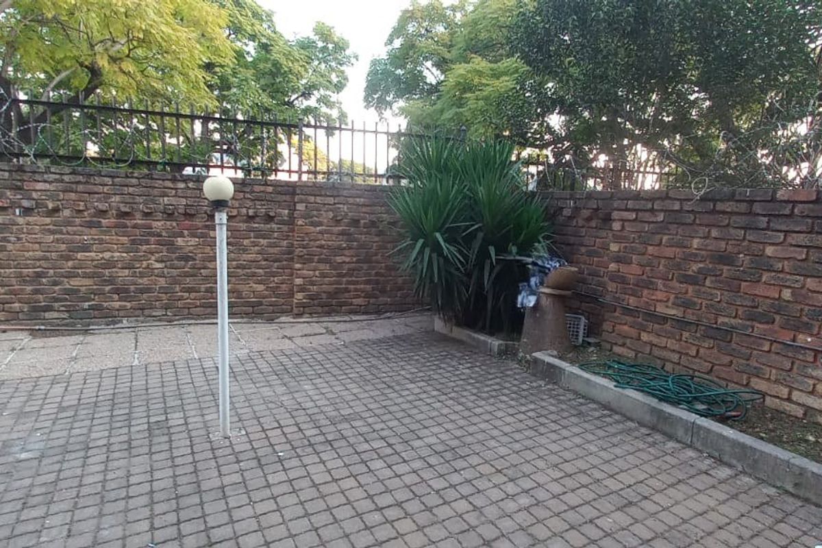 A private rear courtyard featuring a paved patio area enclosed by a high brick boundary wall with security spikes.