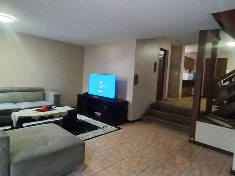 Spacious living room featuring tiled flooring and a prominent wooden staircase leading to the upper level, with an open-plan layout connecting to adjacent areas.