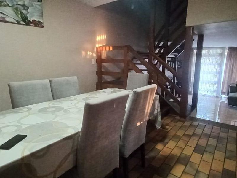 Open plan dining and living area featuring a wooden staircase and tiled flooring, leading to a bright rear living space.